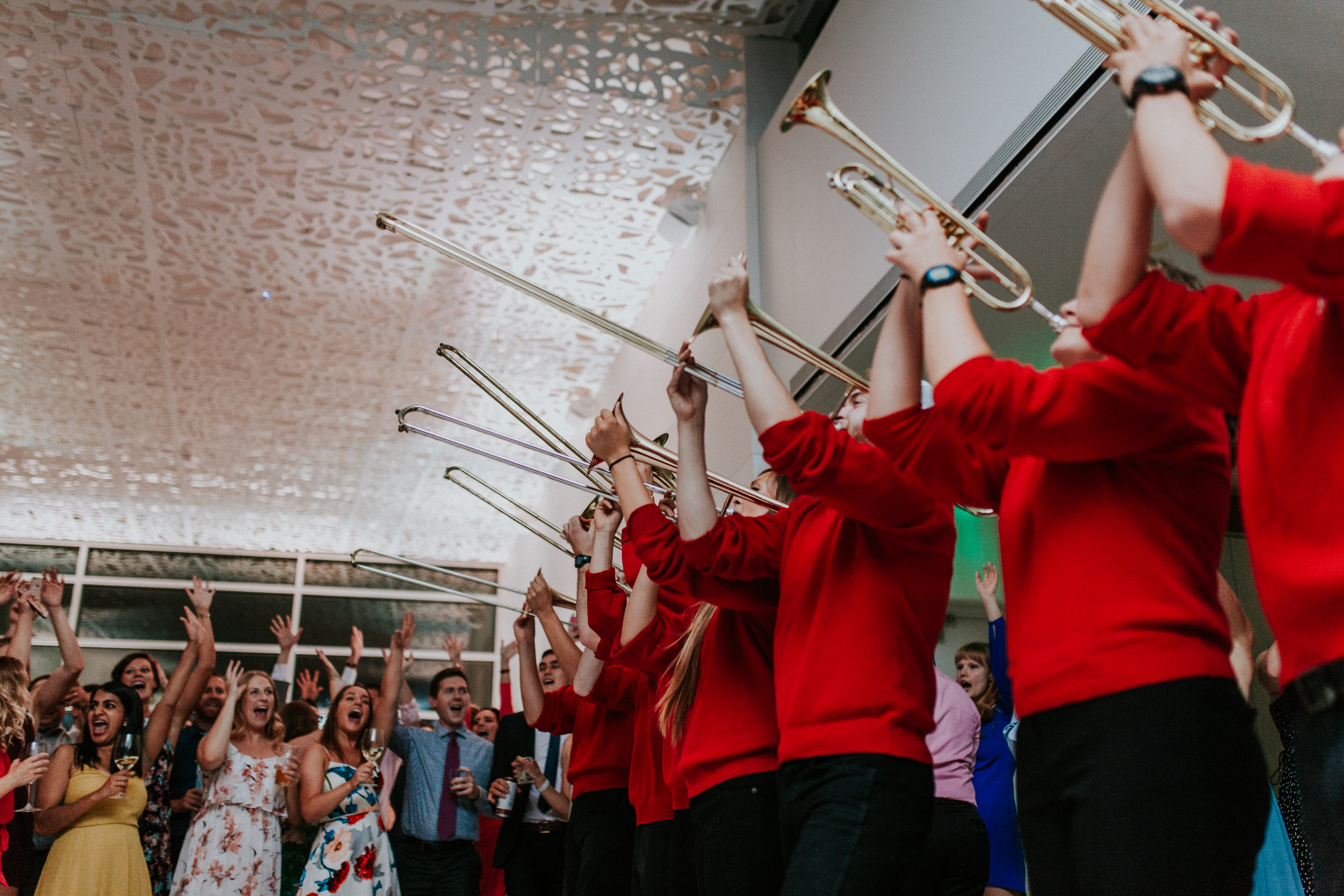 brass band in red playing trumpets in front of wedding crowd