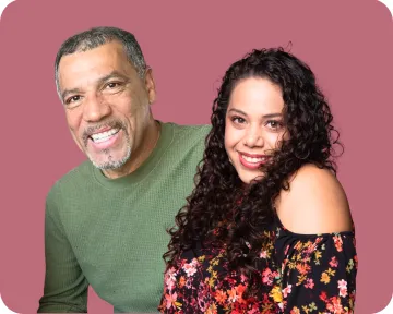 Shelene and Hiram pose together, smiling, in front of a rose colored background